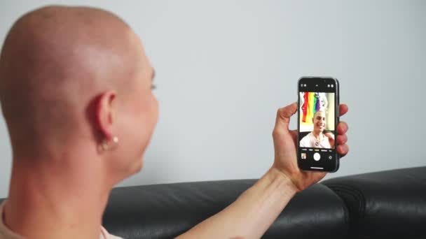 Kafkasyalı kel, altın küpeli eşcinsel bir adam koltukta otururken telefonuyla selfie çekiyor. — Stok video