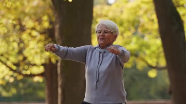 Üst düzey beyaz kadın zıplayarak ellerini parkta spor yapıyor sağlıklı yaşam tarzı aktif yaşlılar konsepti destekliyor — Stok video