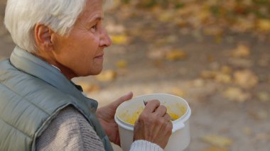  Yaşlı Kafkasyalı kadın parkta çorba içiyor. Gözünü kaçırıyor. Sonbaharda yakın plan seçmeli odak alanı. 
