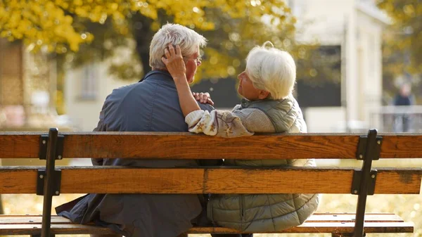 Ältere kaukasische Eheleute sitzen auf der Bank Frau berühren seine Ehemänner Haare lächelnd Medium Schuss von hinten selektiven Fokus — Stockfoto