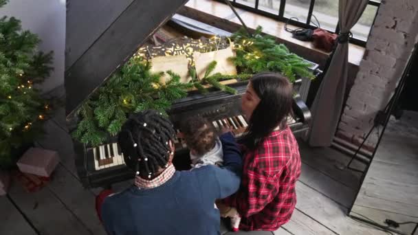 Interraciale familie zit bij de piano, kerstavond te vieren. Mixed-race peuter jongen leren hoe om te spelen op de piano. — Stockvideo