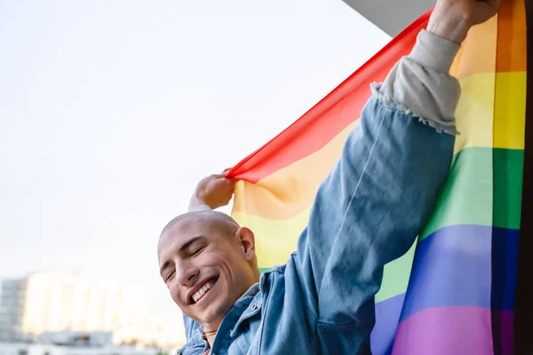 Feliz persona queer no binaria orgullosamente sosteniendo la bandera del orgullo del arco iris y mostrando una sonrisa dentada. Primer plano mediano. —  Fotos de Stock