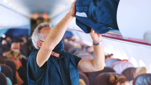 2021.08.18 Mallorca, Spain focus on an elderly man with a mask on his face who puts a travel bag in a box on a plane — Stock Photo, Image
