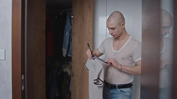 Elegante caucasiano gay homem no um branco malha t-shirt limpeza no seu armário, olhando para seu t-shirts. — Fotografia de Stock