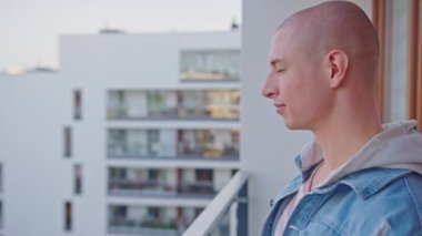 Kafkasyalı kel bir adam balkonda kollarını uzatıyor ve gülümsüyor..