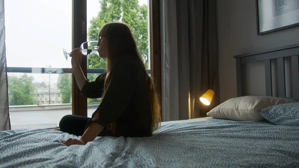 Alkoholmissbruk. Ensam ledsen kaukasiska långhåriga kvinna dricka ett annat vinglas medan du sitter på en säng. — Stockfoto