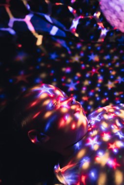 Yıldız projektör lambasına bakan bir çocuğun dikey çekimi. Renkli ışık yıldızlarıyla kaplı..