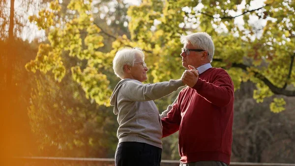 Two elderly caucasian seniors - man and woman - dancing vigorously in their favorite park. Leisure time activities. Active retirement concept. —  Fotos de Stock