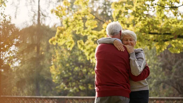 Europäisches älteres grauhaariges Rentnerpaar, das sich nach einem spontanen Tanz im Park umarmt. Herbststimmung. — Stockfoto