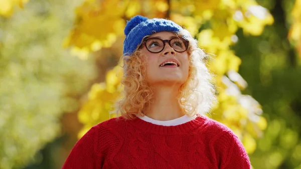 Mittlere Nahaufnahme Millennial blond gelockte Frau mit blauer Mütze und Brille, schaut nach oben Park Hintergrund Kopierraum — Stockfoto