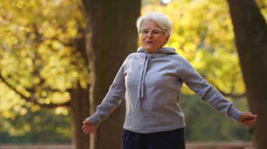 Fitness concept. Being physically active in the old age pays off. Outdoor shot of caucasian pensioner lady in gray hoodie jogging.