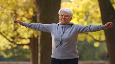 Emeklilik süresince sağlıklı bir yaşam tarzı. Sonbahar parkında egzersiz yapan yaşlı, kır saçlı bir büyükanne. Yüksek kalite fotoğraf