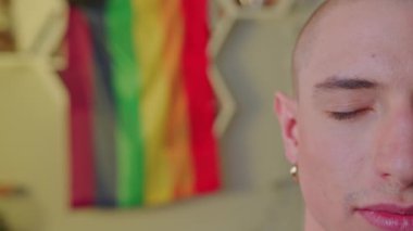 Kulağında küpe olan ve yavaşça gözünü açan Avrupalı kel eşcinsel bir adamın kapalı çekim görüntüsü. Arka planda gökkuşağı bayrağı. Yüksek kalite 4k görüntü