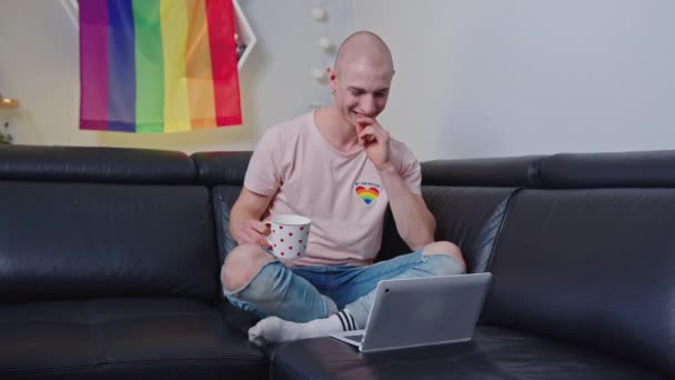 Szczęśliwy Uśmiechnięty Homoseksualny Łysy Biały Mężczyzna Siedzący Czarnej Kanapie Trzymający — Wideo stockowe