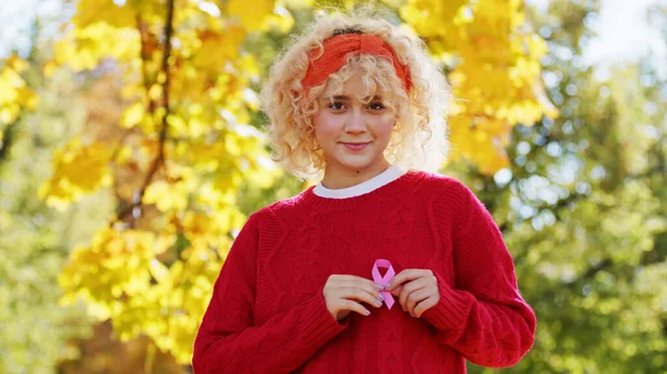 Young blond curly haired woman holds pink ribbon breast cancer support concept copy space outside Pink October — Stockfoto