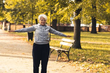 Yaşlı emekli Avrupalı gri saçlı bayan açık havada egzersiz yaparak sağlığına dikkat ediyor. Yaşlılar arasında canlılık ve güç.