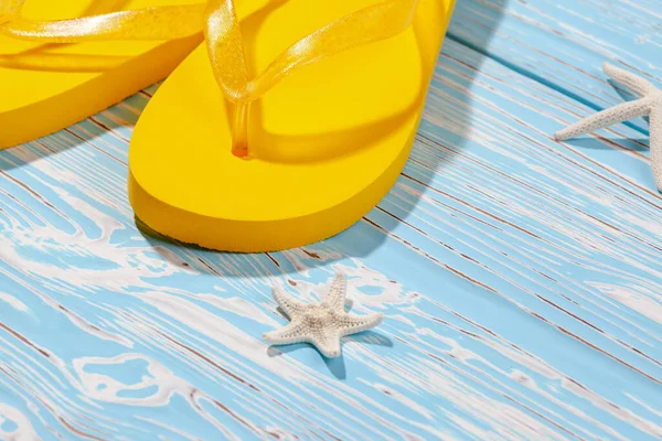 Sarı kauçuk plaj terlikleri ve mavi ahşap arka planda deniz yıldızı, metnin altına.