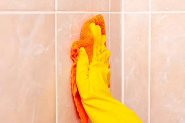 Mano en un guante de goma amarillo limpia las baldosas en el baño — Foto de Stock