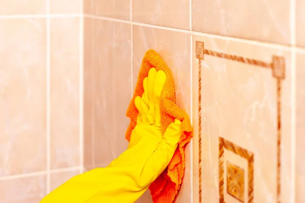 Mano en un guante de goma amarillo limpia las baldosas en el baño —  Fotos de Stock