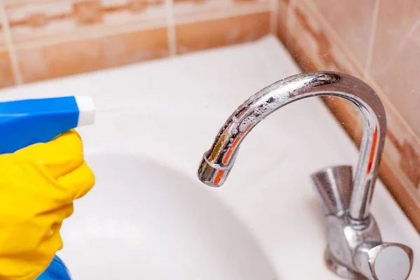 Рука в жовтій гумовій рукавичці дезінфікує водяний кран у ванній — стокове фото