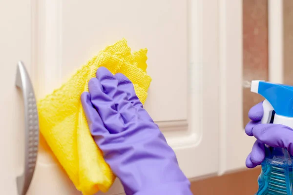 Female hand in a purple rubber glove wipes the beige kitchen cabinet door. Yellow rag in hand — Stock Photo, Image