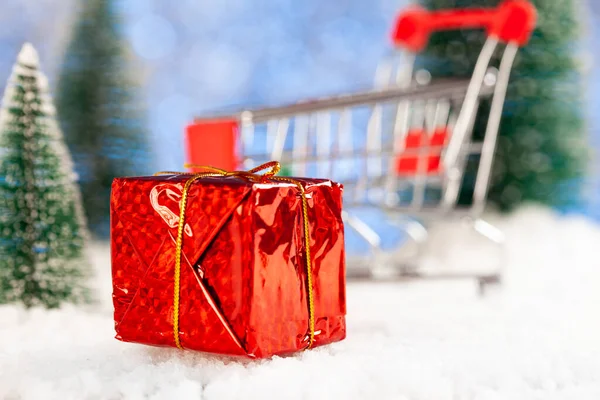 新年の買い物。スーパーマーケットのトロリーを背景にギフト付きの赤い箱。おもちゃのモミの木の周り — ストック写真