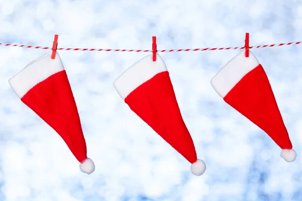 Tres sombreros rojos de Navidad cuelgan de una cuerda contra un fondo azul-gris borroso y brillante. Copiar espacio. Concepto — Foto de Stock