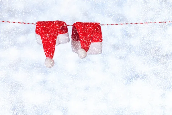 Dos sombreros rojos de Navidad cuelgan de una cuerda sobre un fondo azul-gris borroso y brillante. Copiar espacio. Concepto — Foto de Stock
