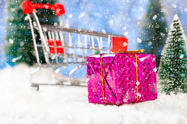 クリスマス・ショッピング。スーパーマーケットのトロリーを背景にギフト付きの紫色のボックス。おもちゃのモミの木の周り — ストック写真