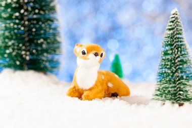 Küçük oyuncak geyik karda oturur. Oyuncak köknar ağaçları. Yeni yıl tebrik kartı