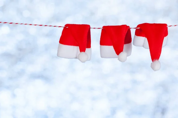 Tres sombreritos rojos de Navidad cuelgan de una cuerda sobre un fondo azul grisáceo borroso y brillante. Copiar espacio, concepto — Foto de Stock