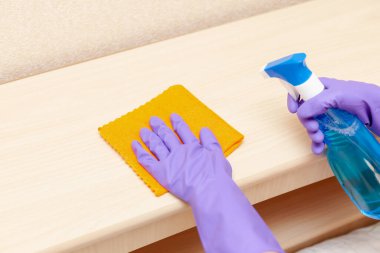 Mor kauçuk eldivenli bir el ahşap bir rafı siliyor.