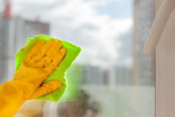 Ręka w żółtej gumowej rękawicy wyciera okno z bliska — Zdjęcie stockowe