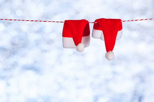 Dos sombreros rojos de Navidad cuelgan de una cuerda sobre un fondo azul-gris borroso y brillante. Copiar espacio. Concepto — Foto de Stock