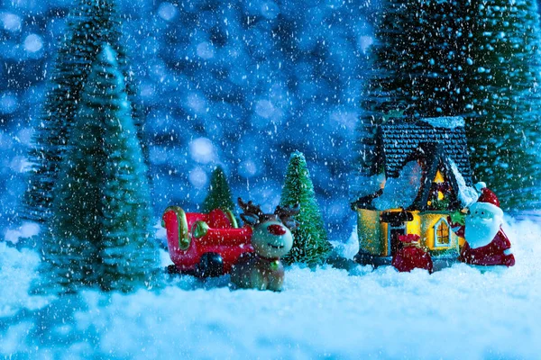 Papai Noel em um trenó perto da casa da aldeia, está nevando, noite. Ano Novo cartão de saudação, conceito — Fotografia de Stock