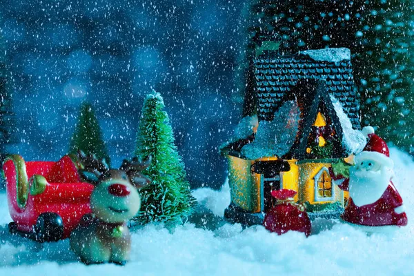 Weihnachtsmann auf einem Schlitten in der Nähe des Dorfhauses, es schneit, Nacht. Neujahrsgrußkarte, Konzept — Stockfoto