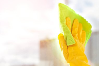 Sarı bir eldiven ile pencereyi siliyor.