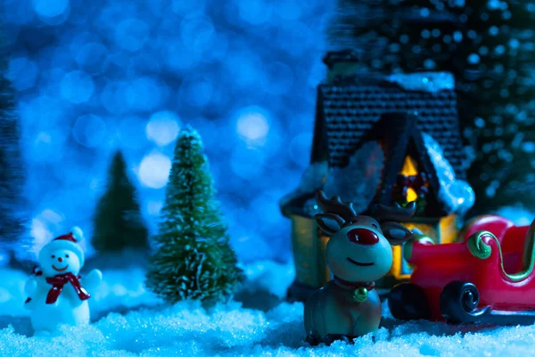Weihnachtsmann auf einem Schlitten in der Nähe des Dorfhauses, es schneit, Nacht. Neujahrsgrußkarte, Konzept — Stockfoto