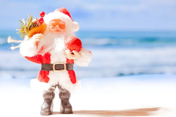 Juguete de Santa Claus en la playa sobre el fondo del mar azul y el cielo azul. Copiar espacio — Foto de Stock