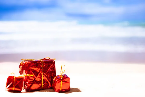 Tres regalos rojos de Año Nuevo en la playa sobre el fondo de la Oseas, espacio de copia. Nuevo año en la playa — Foto de Stock