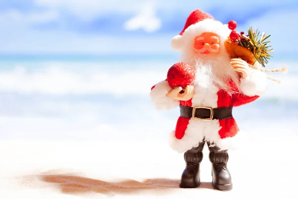 Hračky Santa Claus na pláži na pozadí azurového moře a modré oblohy. Kopírovat prostor — Stock fotografie