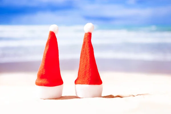 Nowy rok na plaży. Dwa Boże Narodzenie kapelusze na plaży na tle oceanu, przestrzeń kopiowania — Zdjęcie stockowe