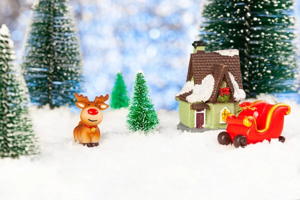 Speelgoed slee en speelgoed rendieren in de sneeuw in de buurt van een klein huis — Stockfoto