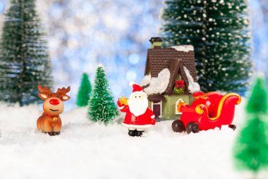 Oyuncak Noel Baba ve karda kızak, etrafta yapay köknar ağaçları, Noel tebrik kartı.