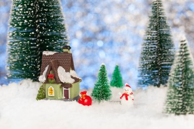 Oyuncak kardan adam hediye dolu bir çantayla küçük bir evin yanında, Noel tebrik kartı.