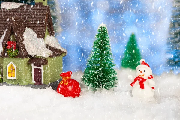 Spielzeug Schneemann mit einem Sack voller Geschenke in der Nähe eines kleinen Hauses, Weihnachtsgrußkarte — Stockfoto