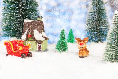 Oyuncak kızak ve oyuncak ren geyiği karda küçük bir evin yanında