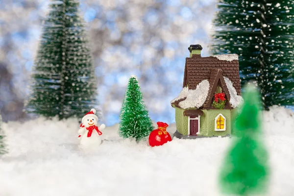 Παιχνίδι χιονάνθρωπος με μια τσάντα με δώρα κοντά σε ένα μικρό σπίτι, Χριστούγεννα ευχετήρια κάρτα — Φωτογραφία Αρχείου