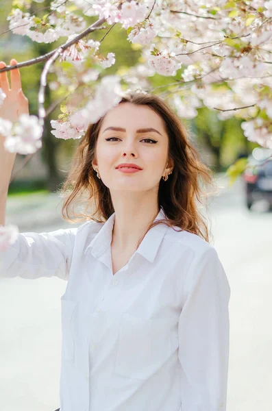 Sakura ağaçlarının yanında beyaz gömlekli bir kız. Sakura çiçekleri. Bahar.