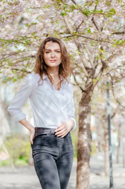 Beyaz gömlekli kız baharda çiçek açan sakura 'nın yanında duruyor.